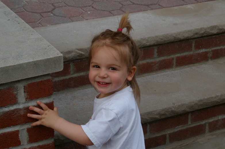 a little girl wearing a pink pigtails smiles while standing on the outside steps of her home