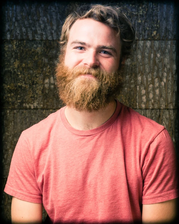 a man with a large beard and a beard standing in front of a wooden wall