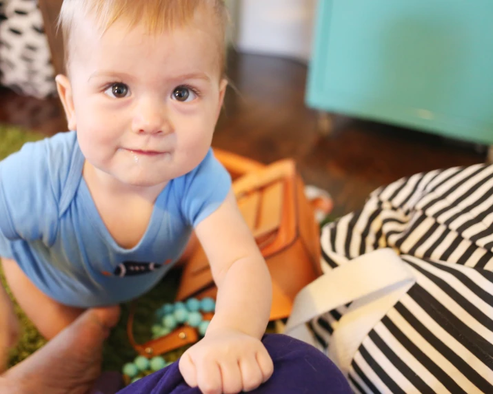 a  sitting on the floor while holding onto a small suitcase