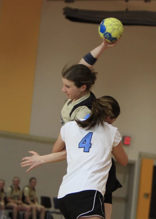 two girls jump together in the air to catch a ball