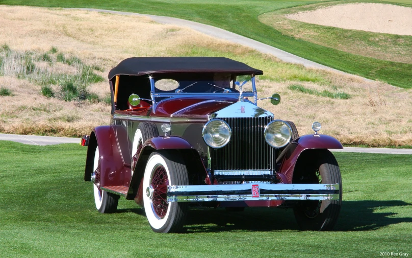 a classic car parked on grass in front of a golf course
