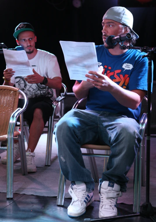 two people sitting in chairs on stage with sheet music