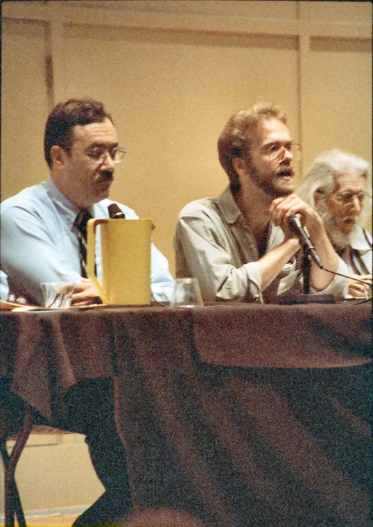 three people sitting at a long table in front of a microphone