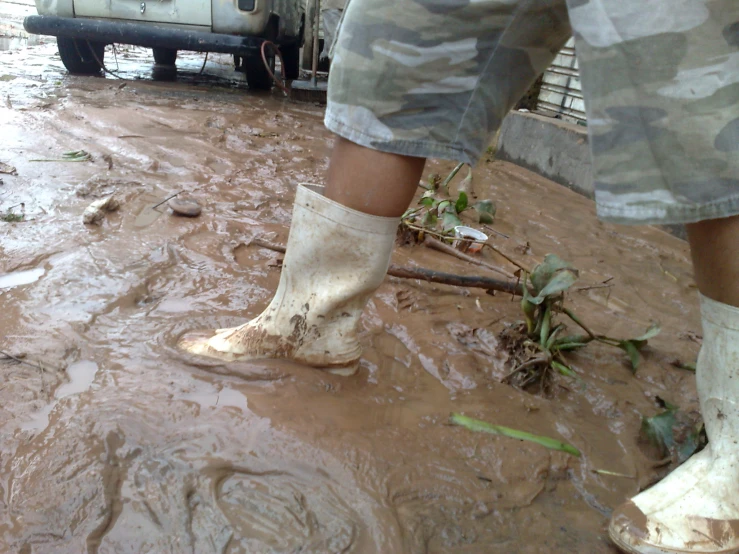 a muddy street and mud is very dirty with a man in white boots standing in it