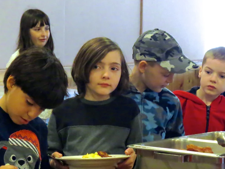 a group of children standing around a counter eating