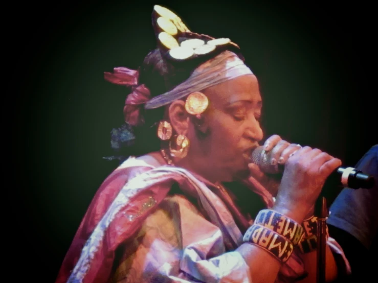 a woman wearing an elaborate headdress holds a microphone in her hand