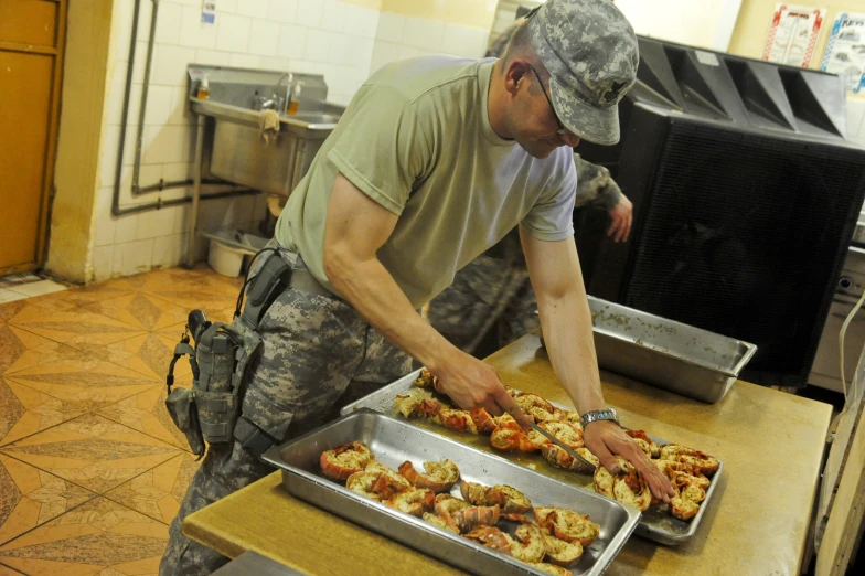 a man wearing fatigues is in front of trays of food