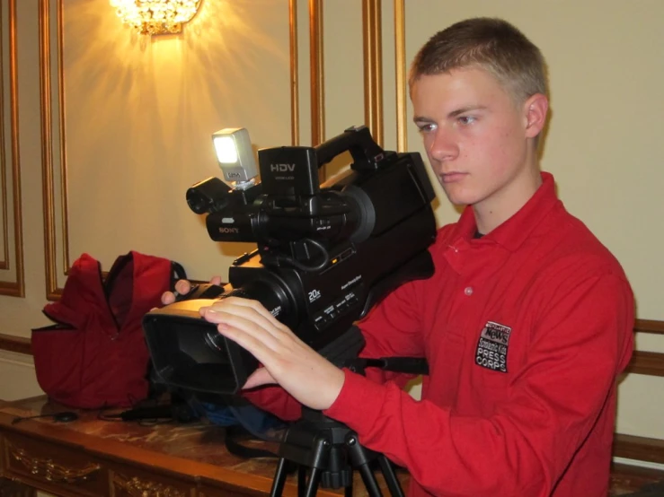 a boy holding a camera near a tripod in a room