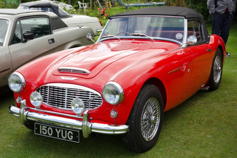 red vintage convertible parked on grass next to several older cars