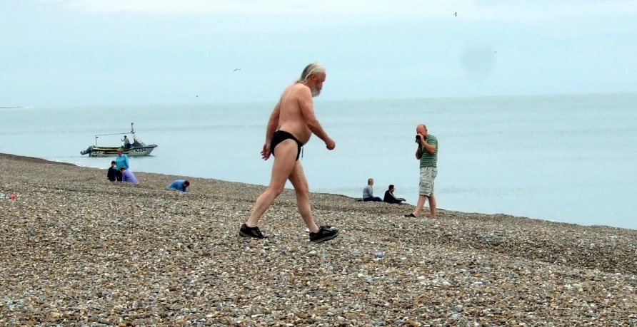 a shirtless older man is walking on the sand