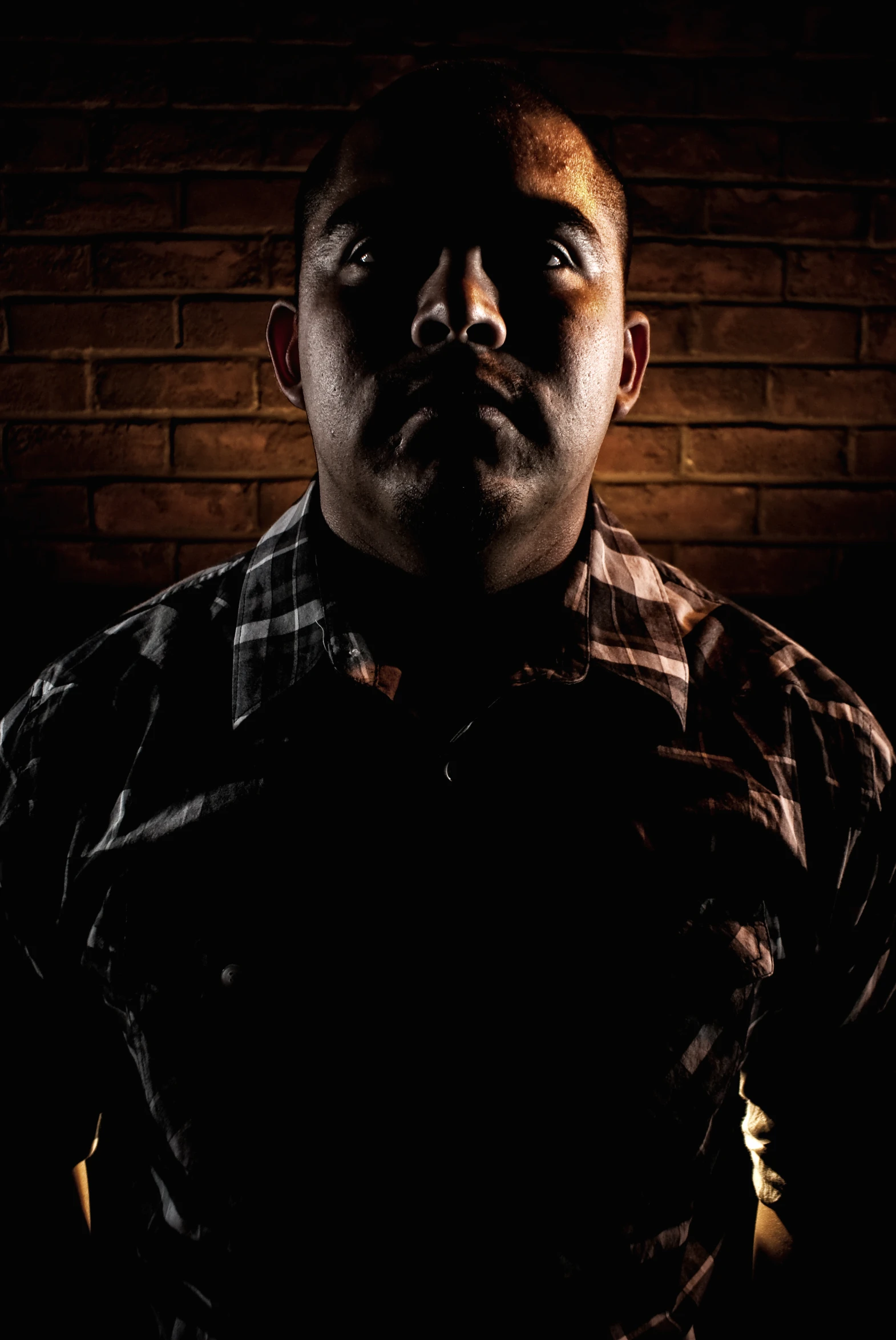 a man in plaid shirt standing by brick wall