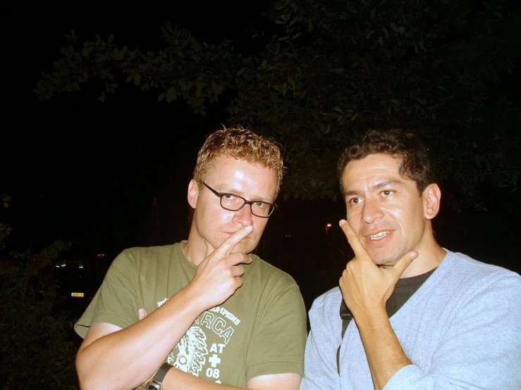 two men sitting together in the dark, posing for the camera
