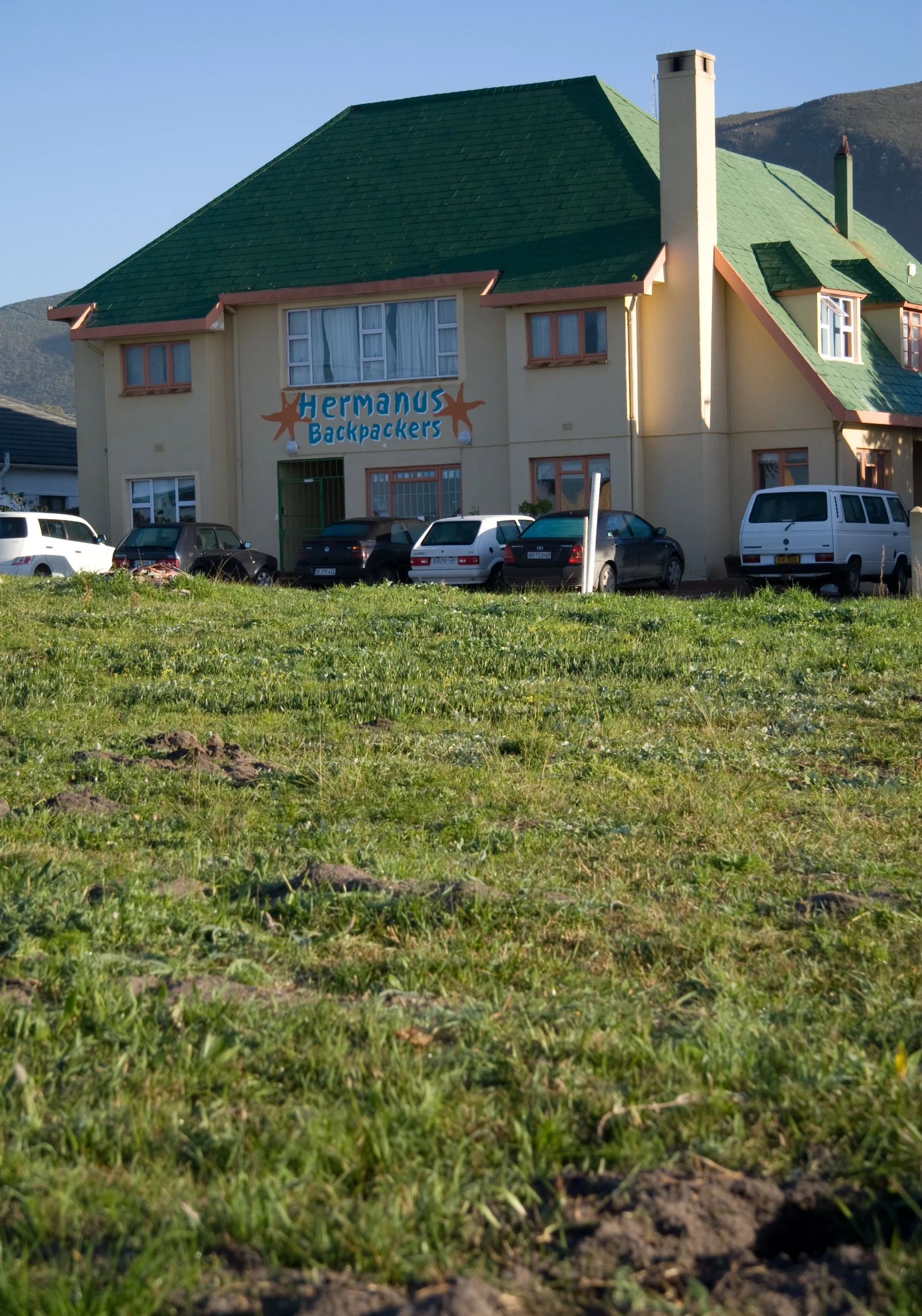 a yellow building with a green roof and parking lot