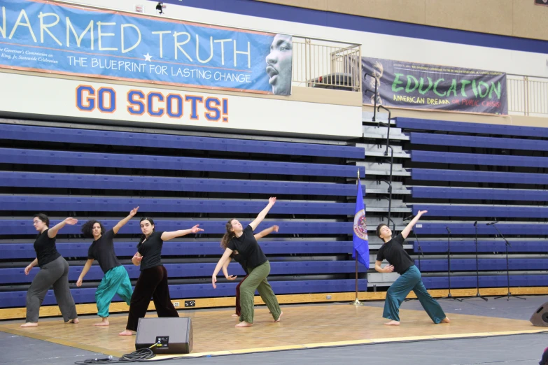 six women are standing on a stage and reaching towards the sky in a yoga position