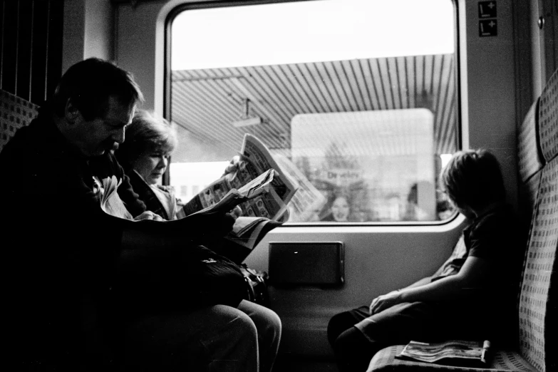 two people are sitting on a train looking at a magazine