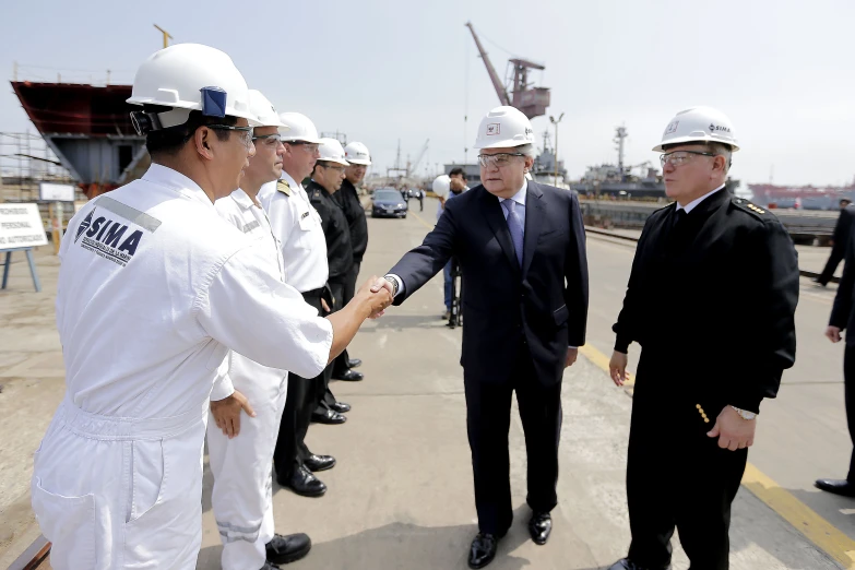 two men in suits shaking hands while two men are standing next to them