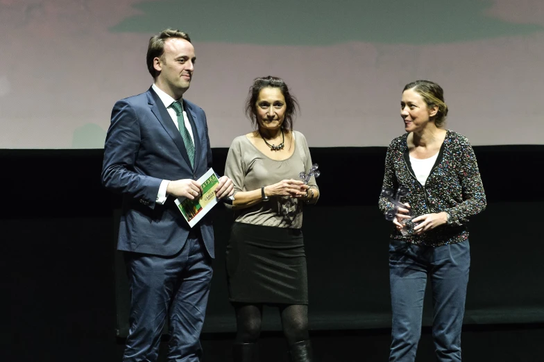 three people on stage stand at the end of a presentation