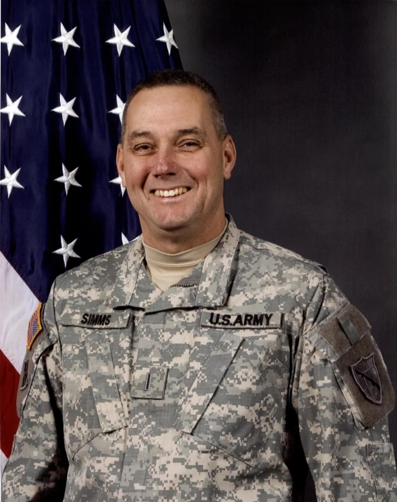 an army soldier smiles while standing in front of an american flag