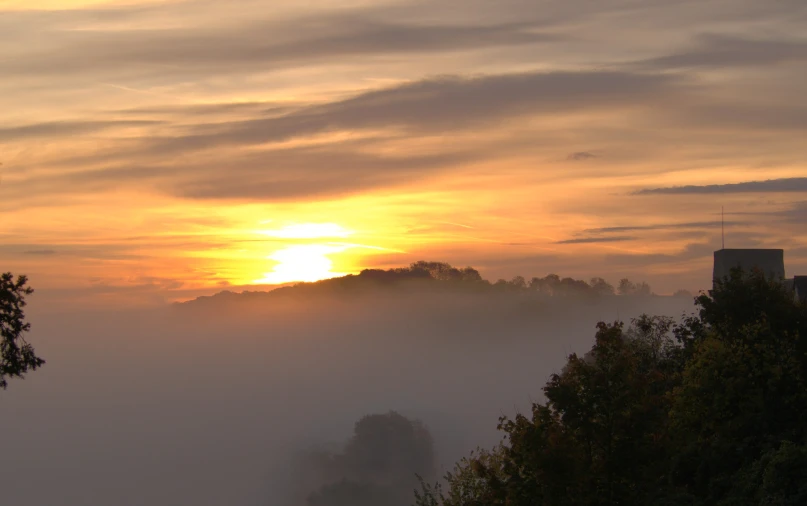 a sun is setting on a foggy evening in the mountains