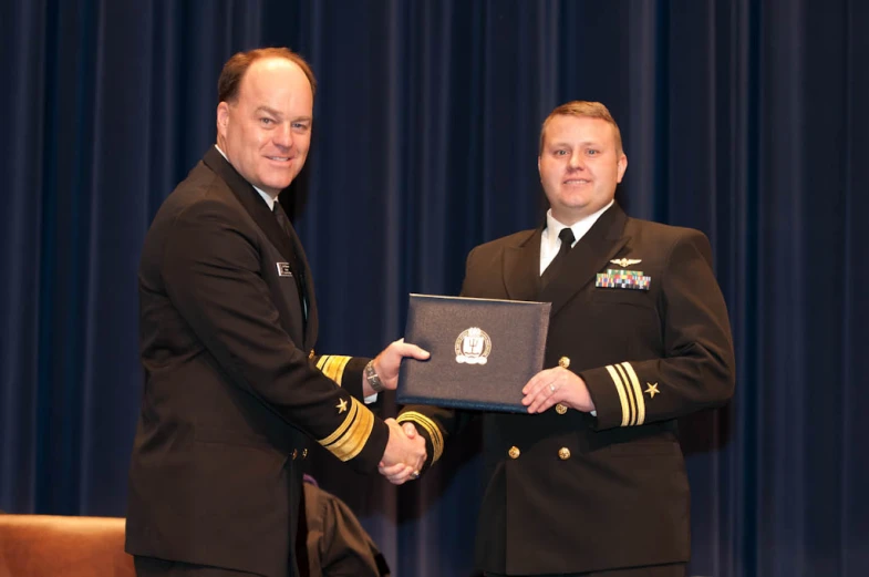 two men in military uniforms hold a plaque