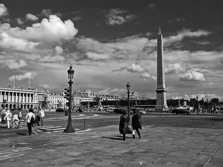 people walking in front of a monument with cars passing by