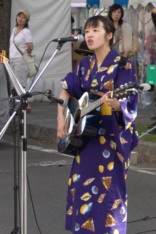 a girl in a purple dress plays an acoustic guitar at an outdoor market
