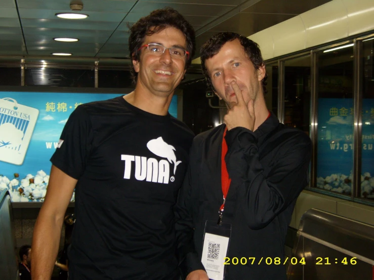 two men pose for the camera in front of a wall