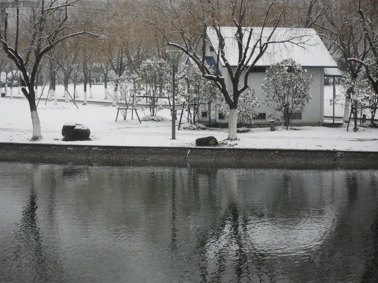 a view of a snow covered park, including a building, and tree lined pond