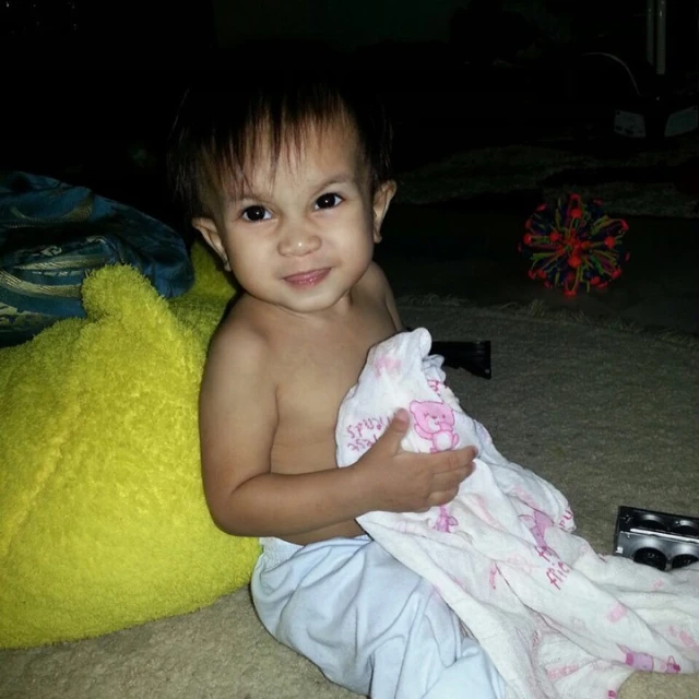 a child sits on the floor and smiles while holding a towel