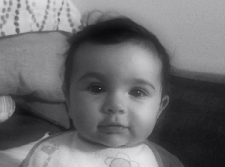 baby with bib looking at camera with stuffed teddy bear toy