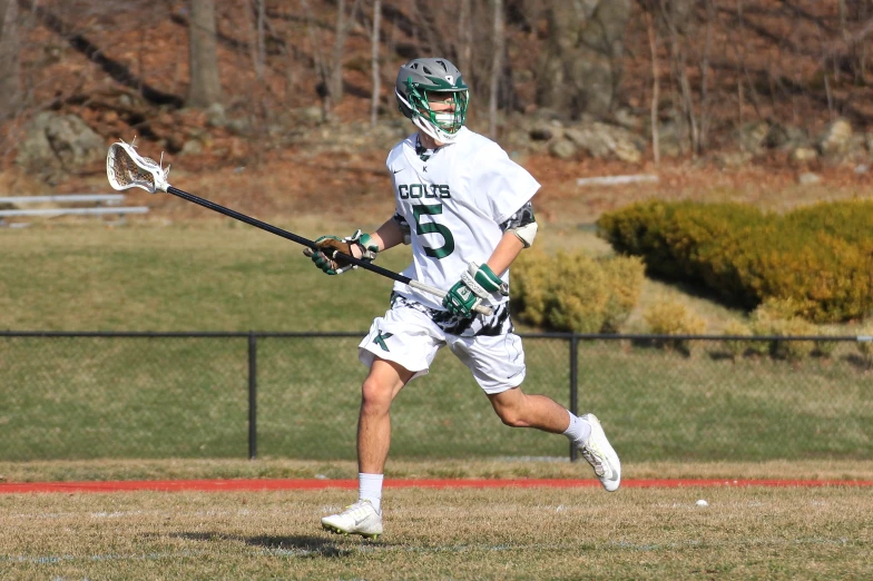 a man in lacrosse uniform runs to the field with his ball