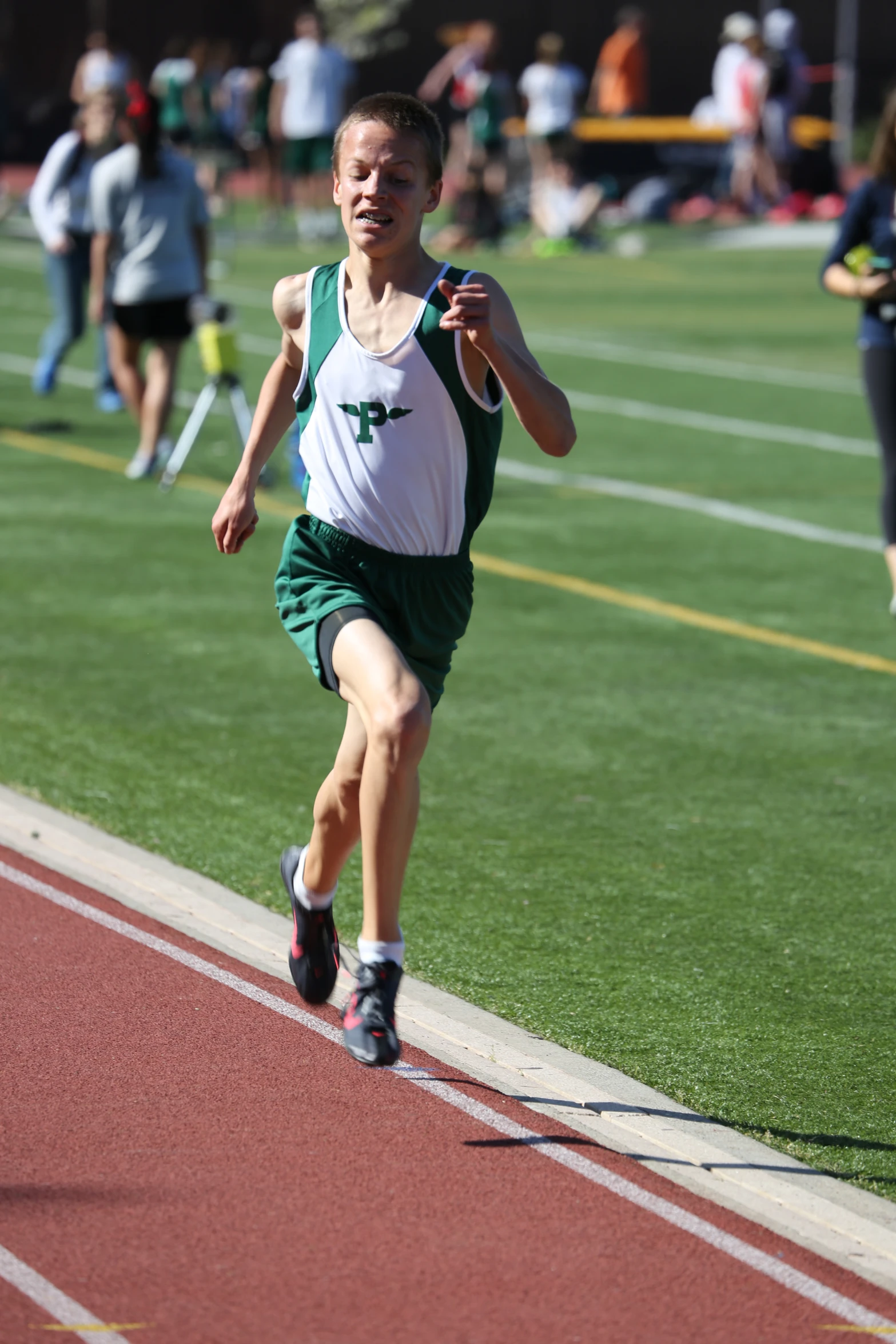 a boy runs along a track in a green and white shirt