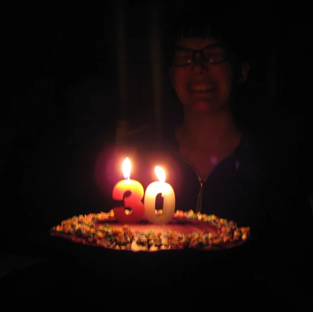 a person standing in front of a birthday cake with lit candles