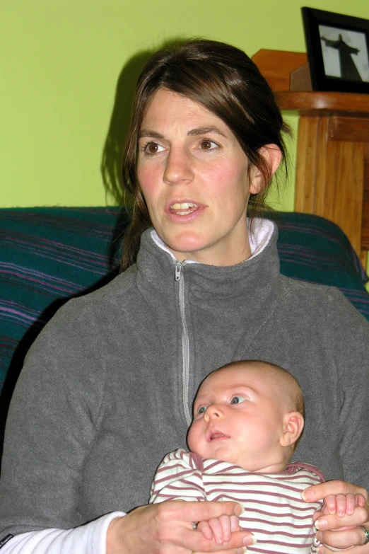 a woman holding a baby next to green wall
