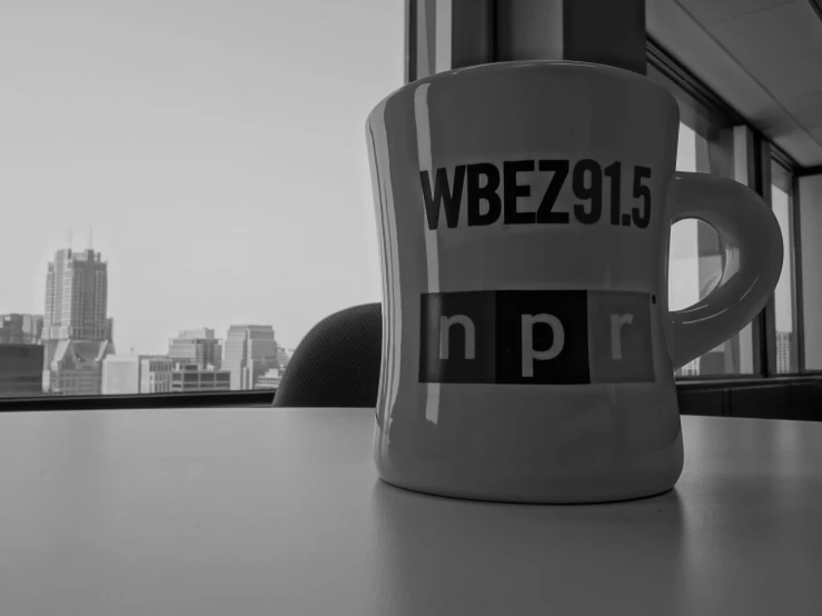 a coffee cup sits on a table beside a window overlooking a city