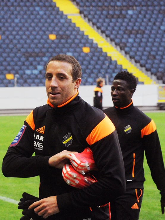 two men in sports uniforms holding balls and walking