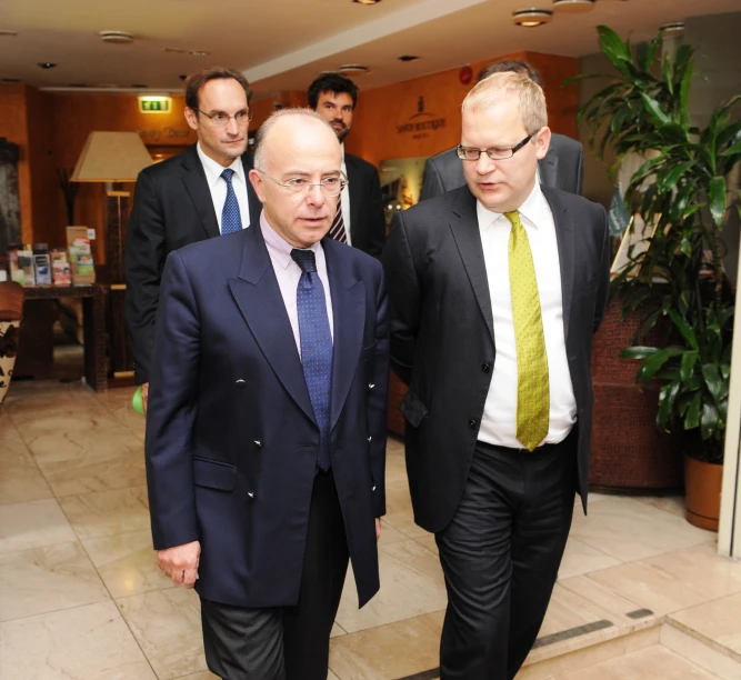 two men wearing suits and tie walking along a lobby