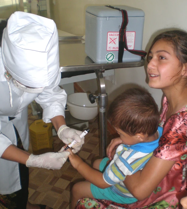 two women in white lab coats helping a child put on gloves