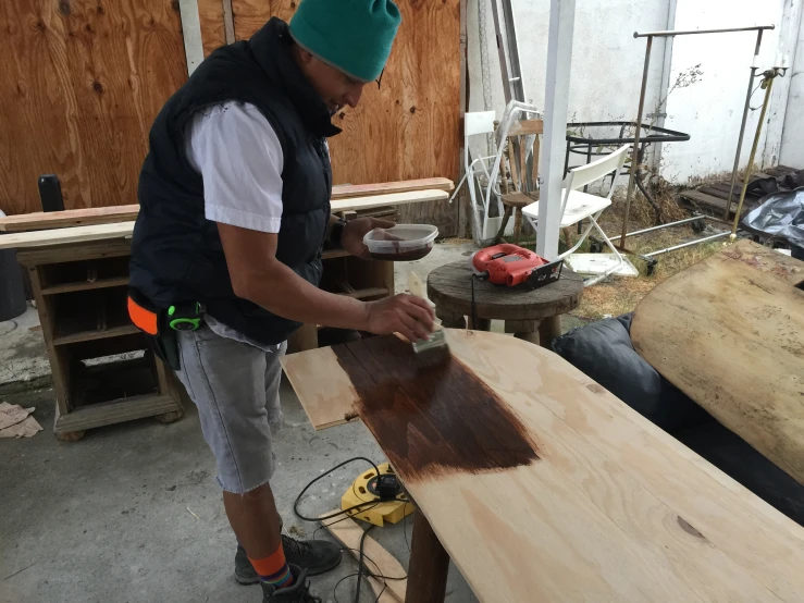 man in a woodworking area working on wooden furniture