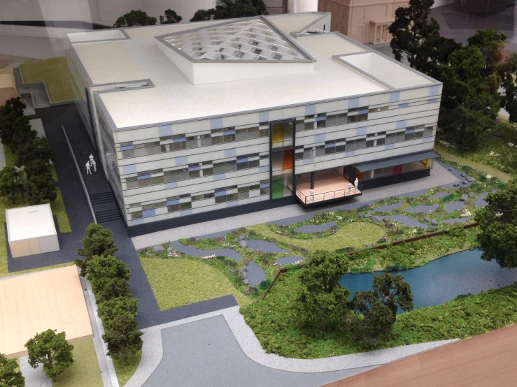 a model of a large building that includes landscaping, trees, and a pond