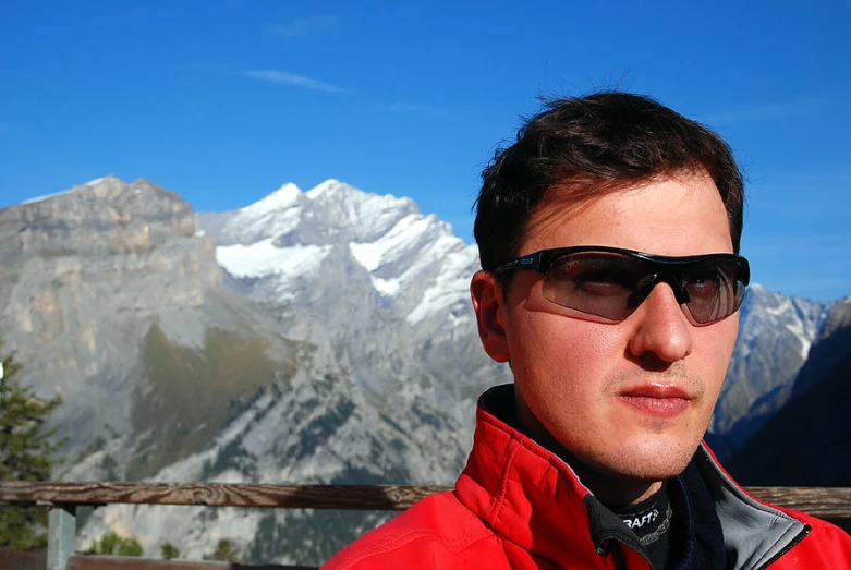 a man wearing sunglasses and sitting on a bench in front of the mountains