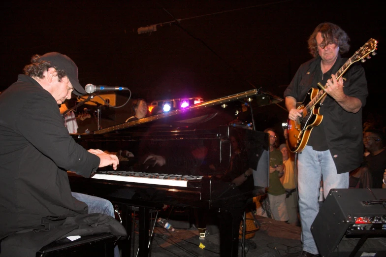 a man with a guitar, standing next to a piano and singing