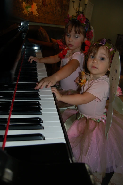 two children in princess costumes playing the piano