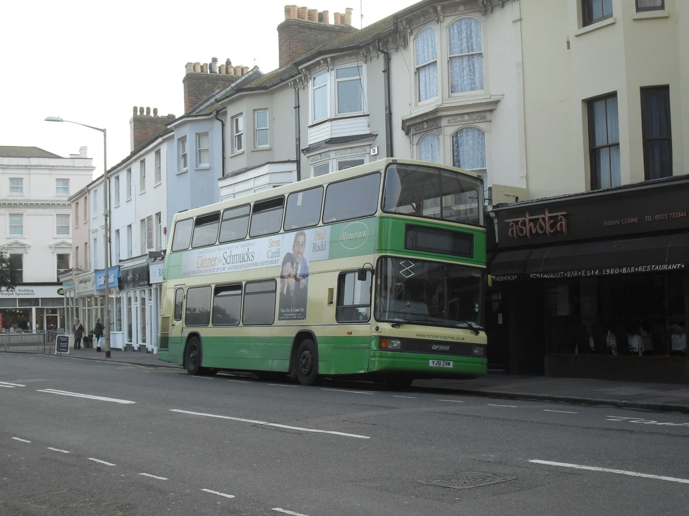 a green double decker bus parked in front of a white building