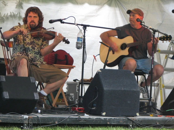 two guys are playing guitar in a grassy area