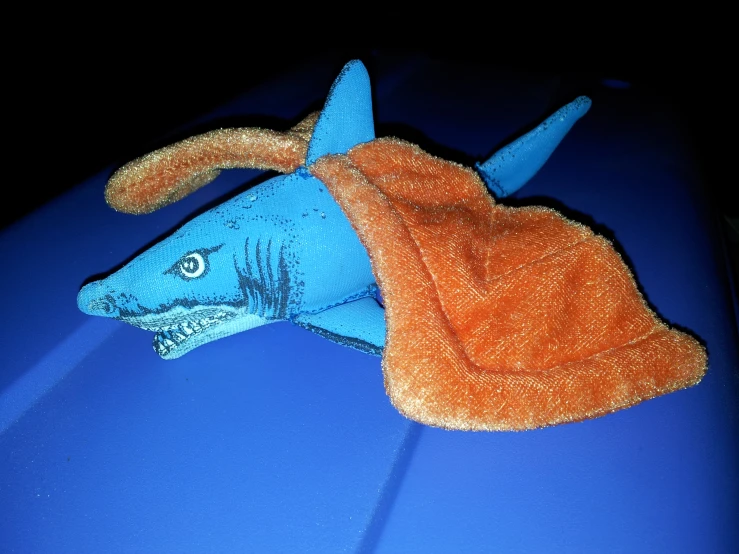 a stuffed shark laying down on top of a blue car