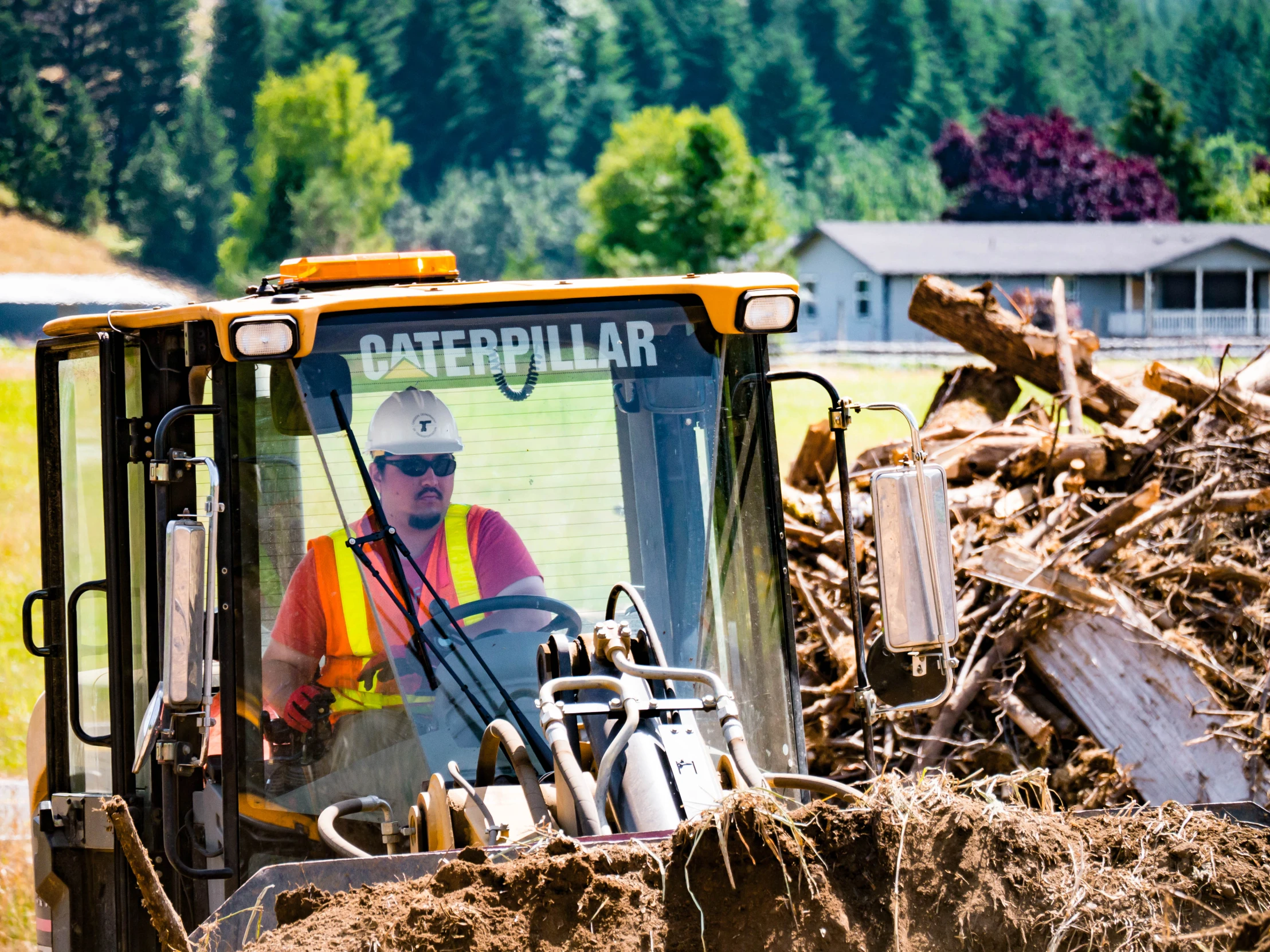 a construction worker drives a tractor through a pile of tree trunks