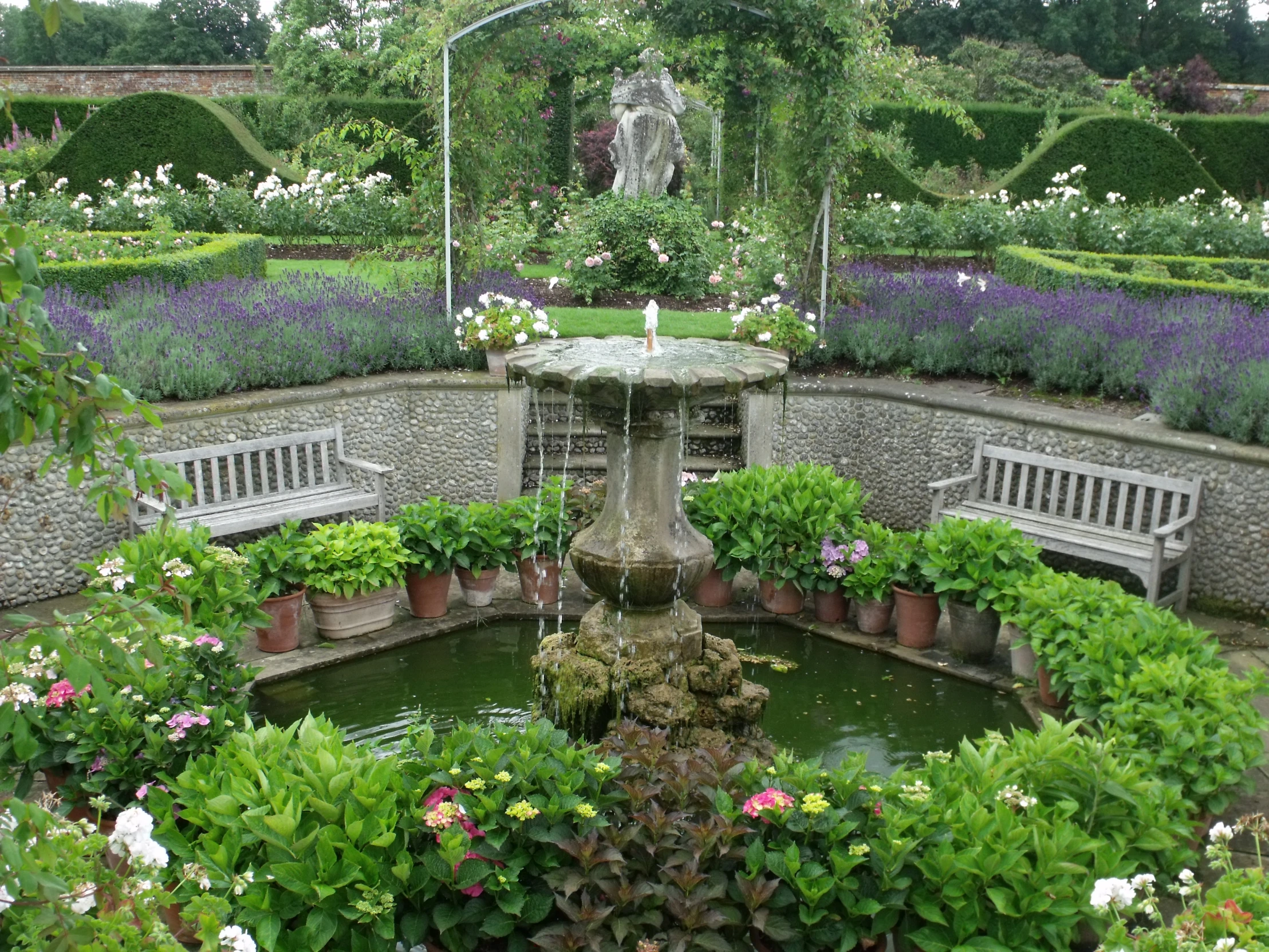 the beautiful garden has a fountain with two benches in it