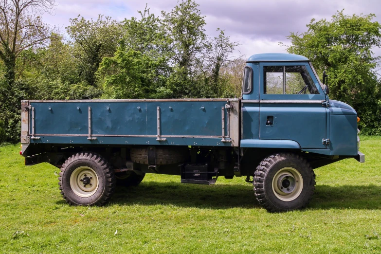 a blue, military style truck parked on top of a lush green field