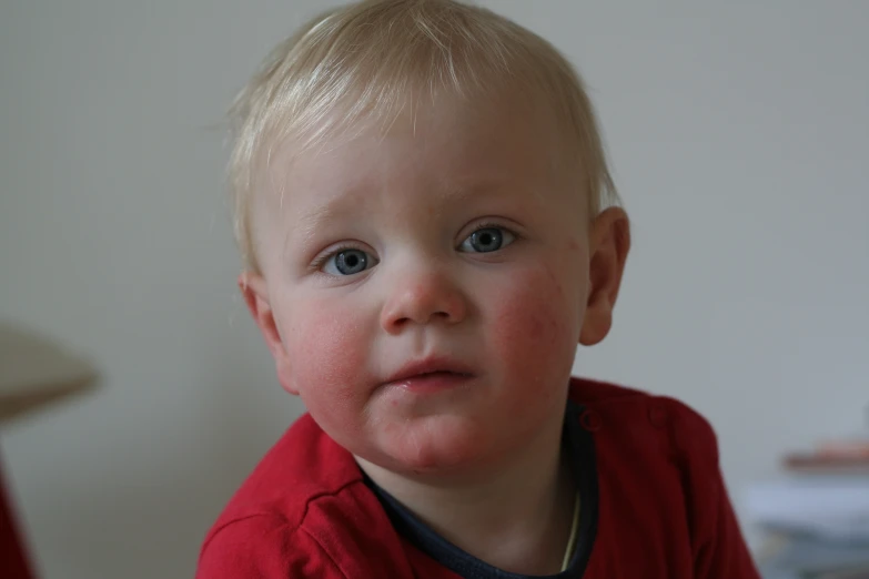 an infant boy looking back while holding onto his shirt